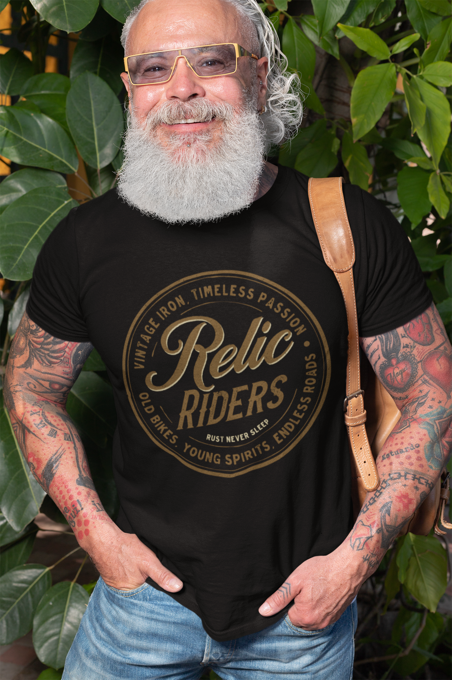 Bearded man wearing Relic Riders Motorcycle T-shirt with vintage logo, standing in front of greenery.